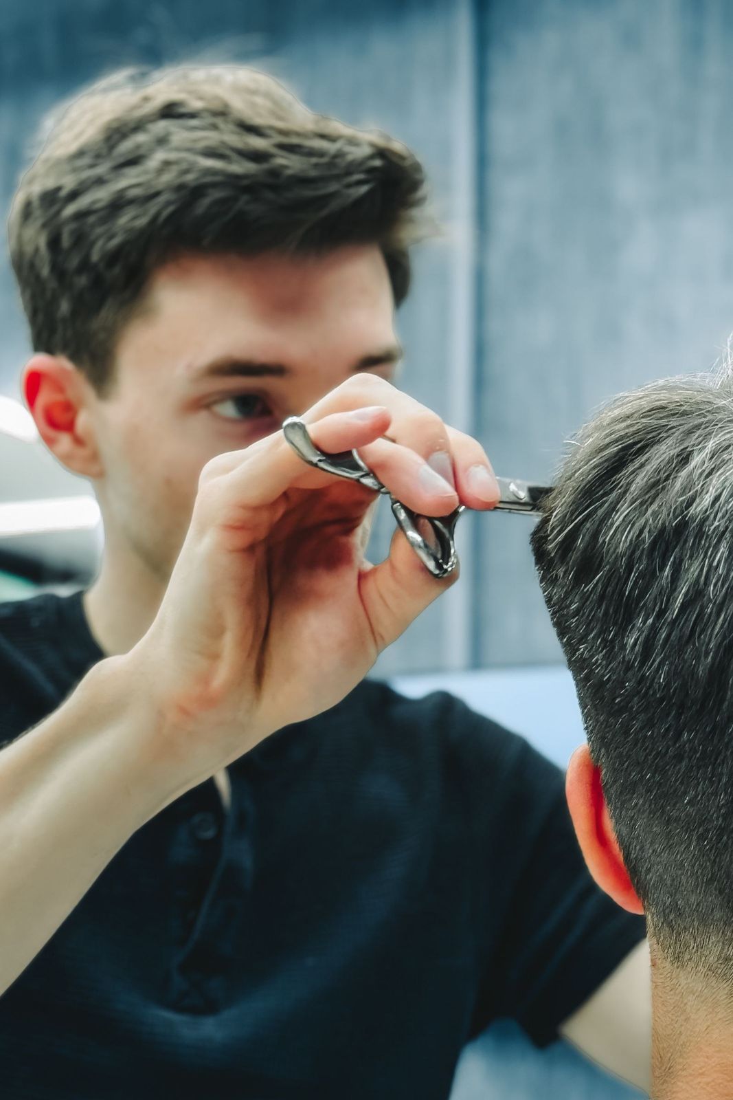 Tesoura aparando o corte, cliente e barbeiro no espelho